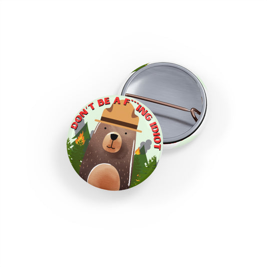 Front and back views of a round pin featuring a brown bear with a ranger hat in front of a forest on fire that says "Don't Be a F***ing Idiot."